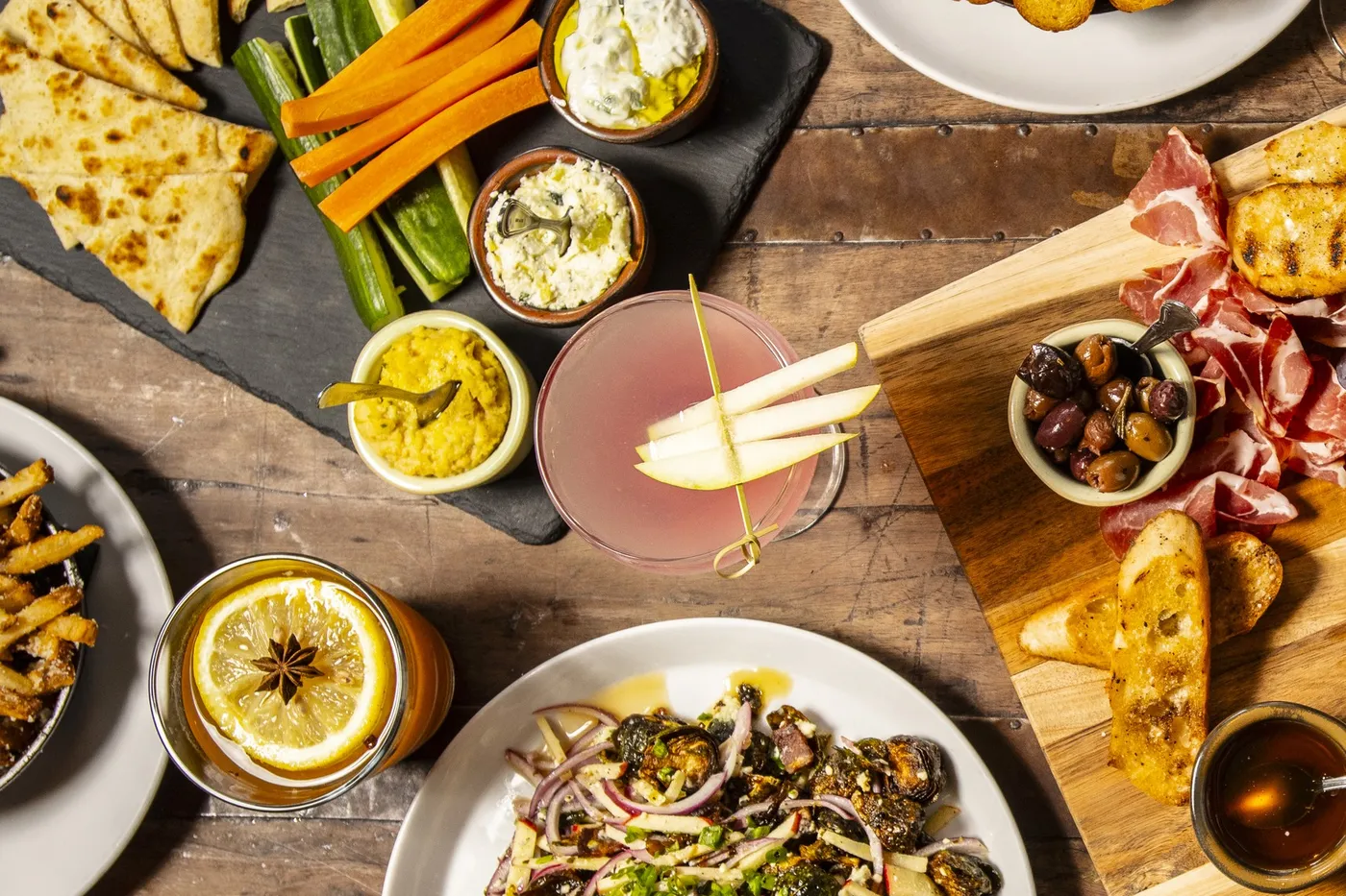 Overhead shot of shareable plates, boards and a cocktail on a wood table at Melzingah Tap House