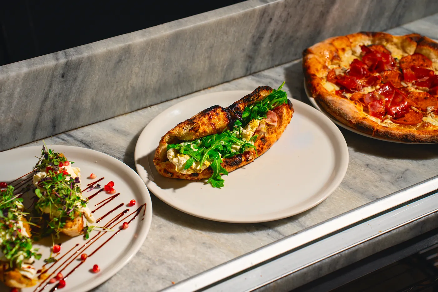 Wood-fired pizza, sandwich and plates on the marble counter at Pizzeria Posto in Eastdale Village