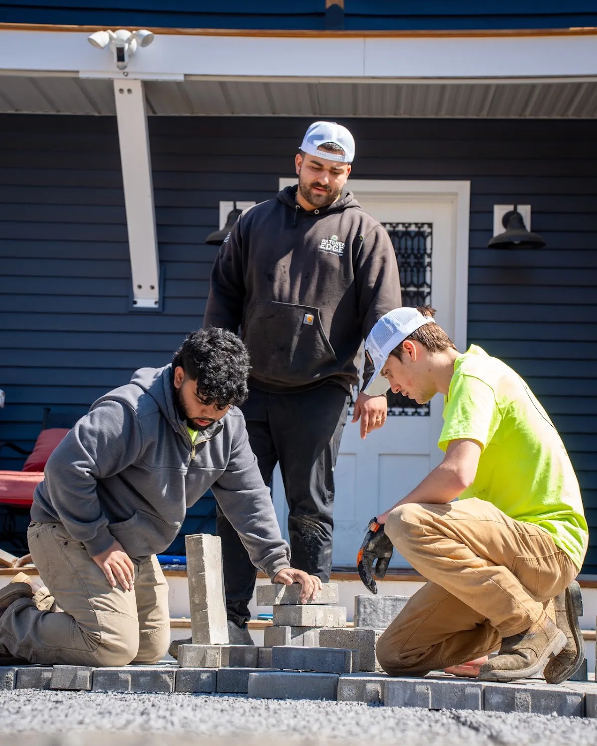 Three-man crew laying pavers by porch, hardscaping photography Hudson Valley