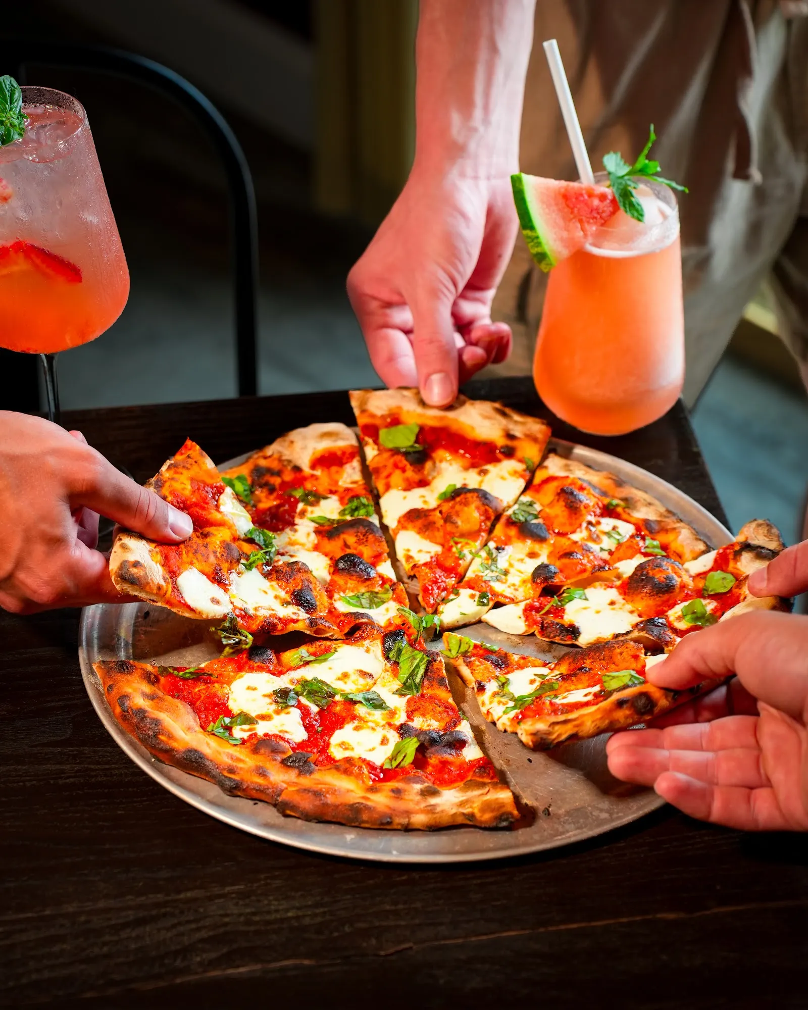 Friends grabbing wood-fired pizza slices with cocktails, restaurant photography Hudson Valley